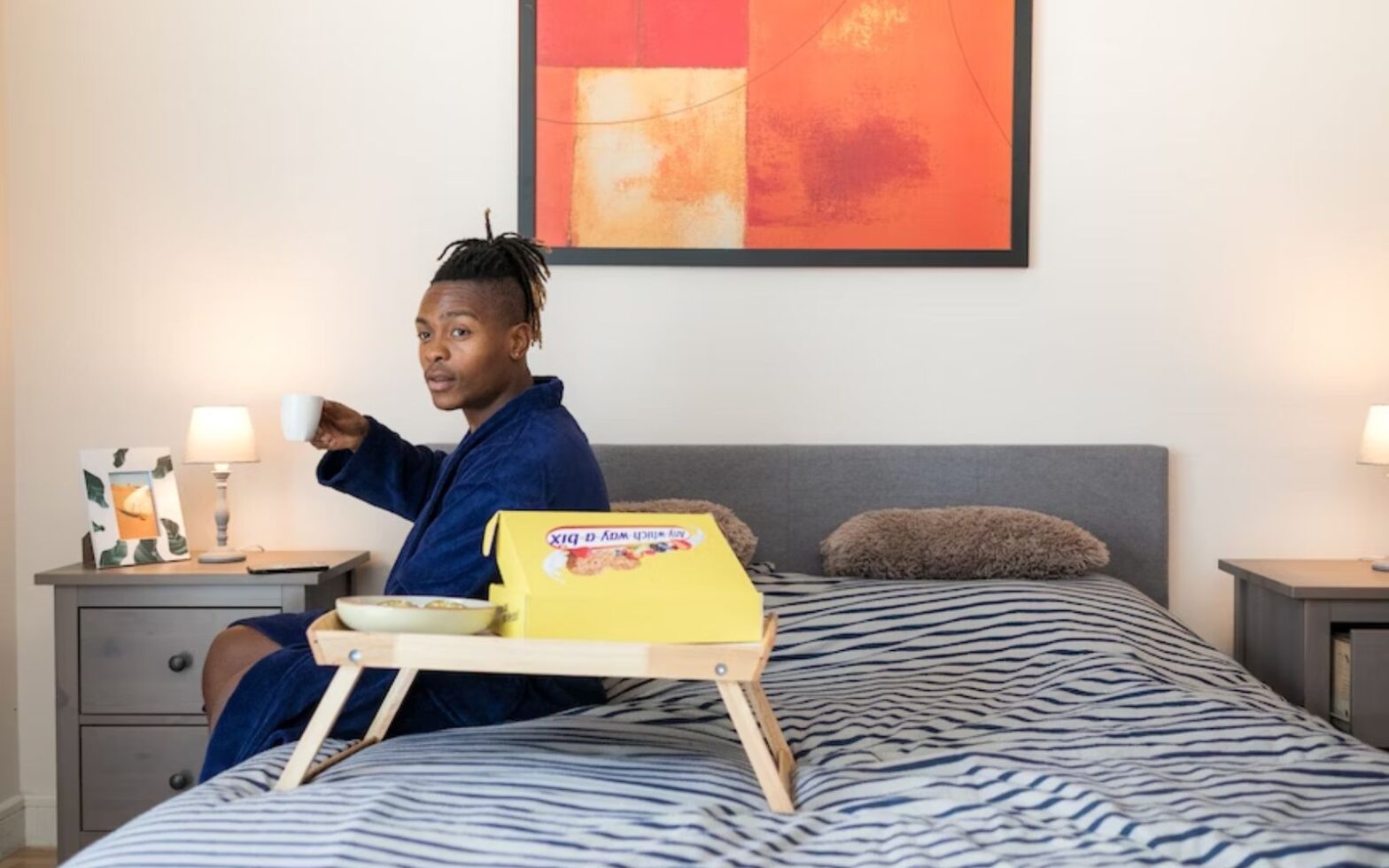 Black man holding a cup of coffee while sitting on the edge of a bed - Top Black-Owned Bed and Breakfasts in the US