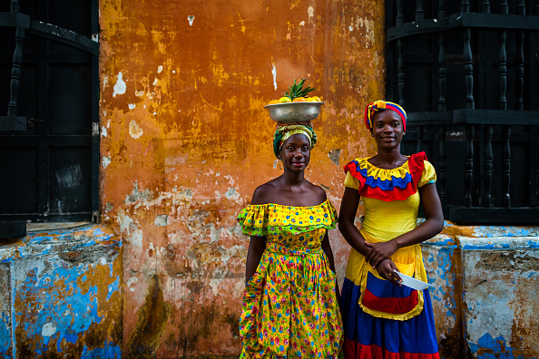 CARTAGENA, COLOMBIA - DECEMBER 12: Afro-Colombian girls, dressed in the traditional palenquera costume, pose for a picture in front of a colonial house in walled city on December 12, 2017 in Cartagena, Colombia. After the peace agreement, ending a 52-year civil conflict and political stability in Colombia, Cartagena de Indias, a UNESCO World Heritage, experiences a tourism boom. The historic landmarks from the Spanish colonial times are being restored, private investments are visible in the city and an increased number of local people benefit from the boom of the travel related service