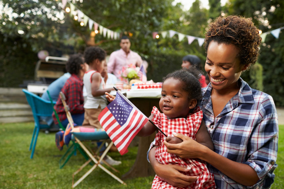 Black mother and daughter holding American flag outdoors at a BBQ