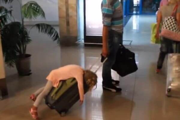 female child sleeping on luggage as dad wheels her through the airport