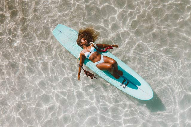Black woman laying on surfboard in the water