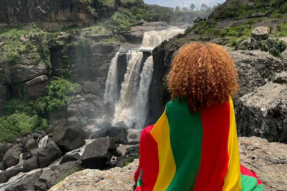 woman draped in flag of Ethiopia sitting near a waterfall