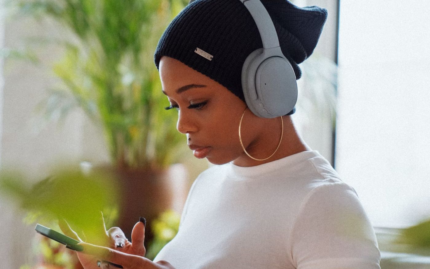 woman scrolling on cell phone while wearing headphones - best headphone under 200 list