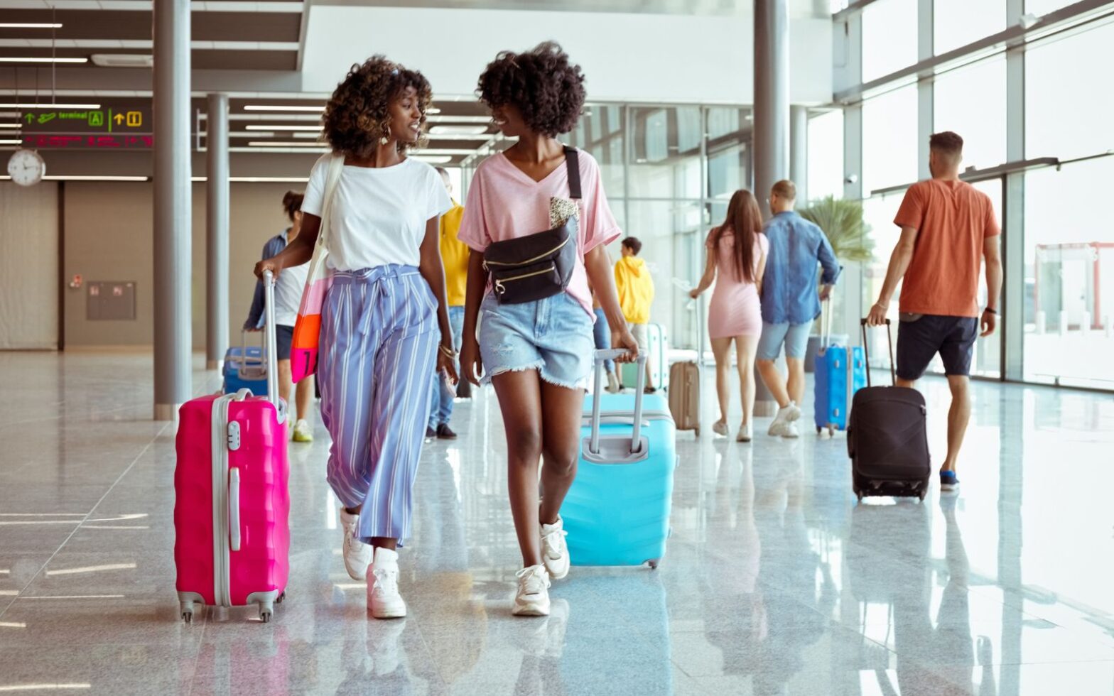 two young Black women walking through the airport with luggage - Gen Z travelers