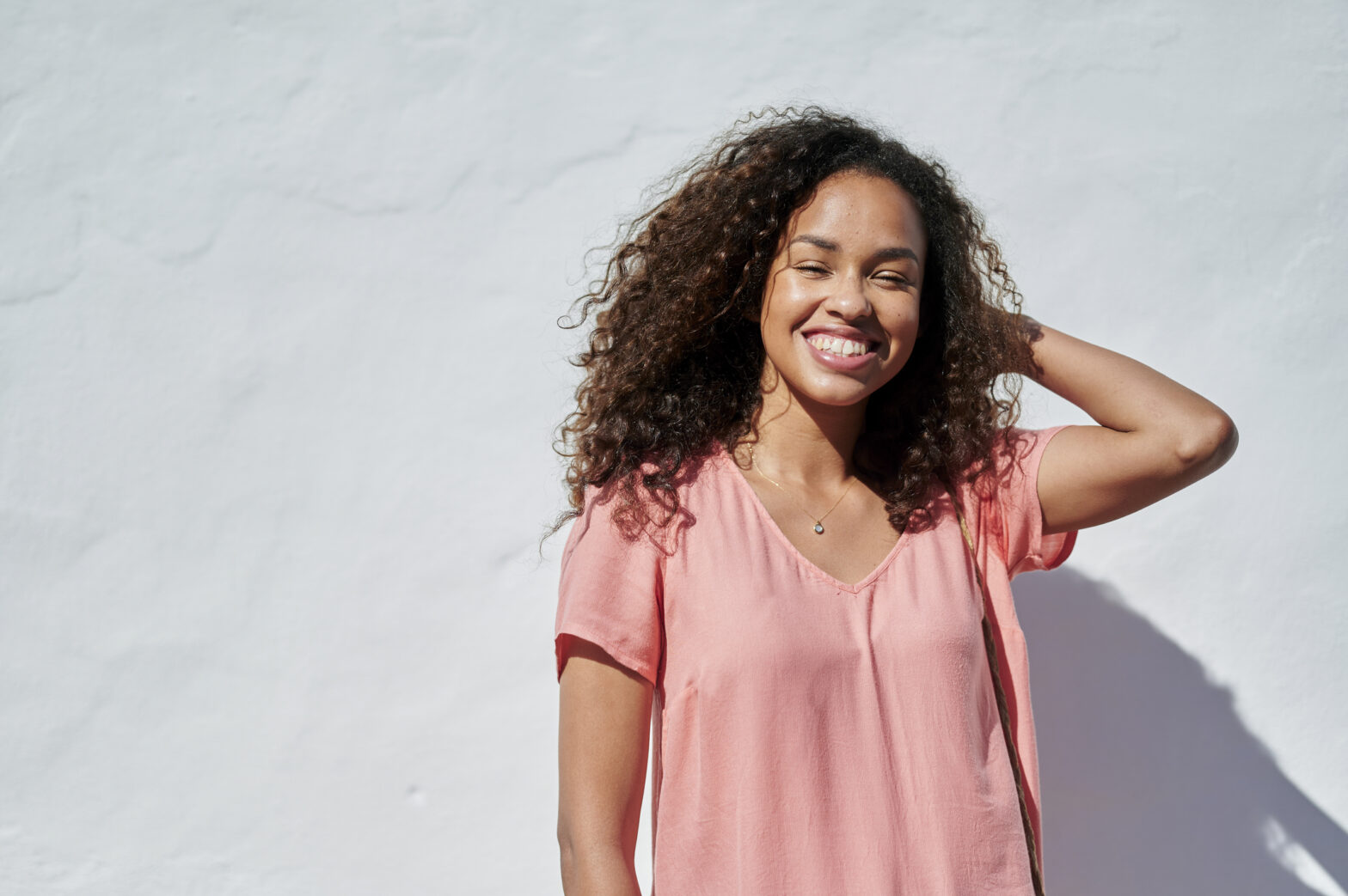 Portrait of smiling woman with curly hair in front of white wall