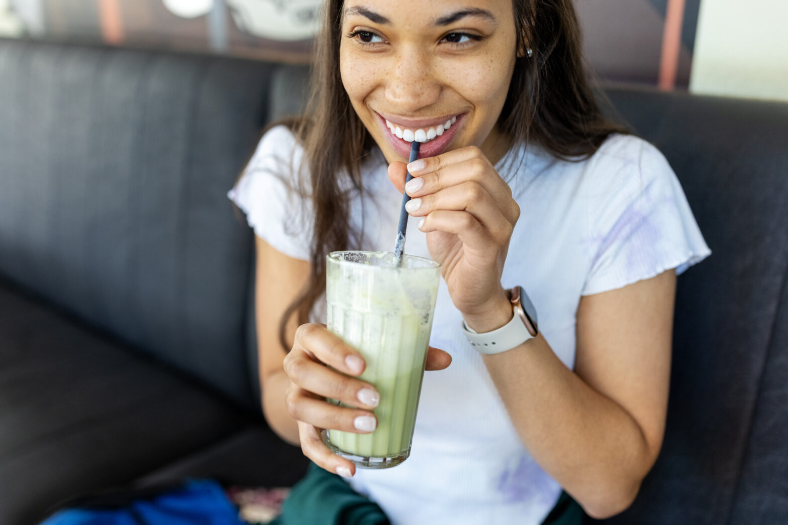 Happy young woman having iced matcha latte at cafe