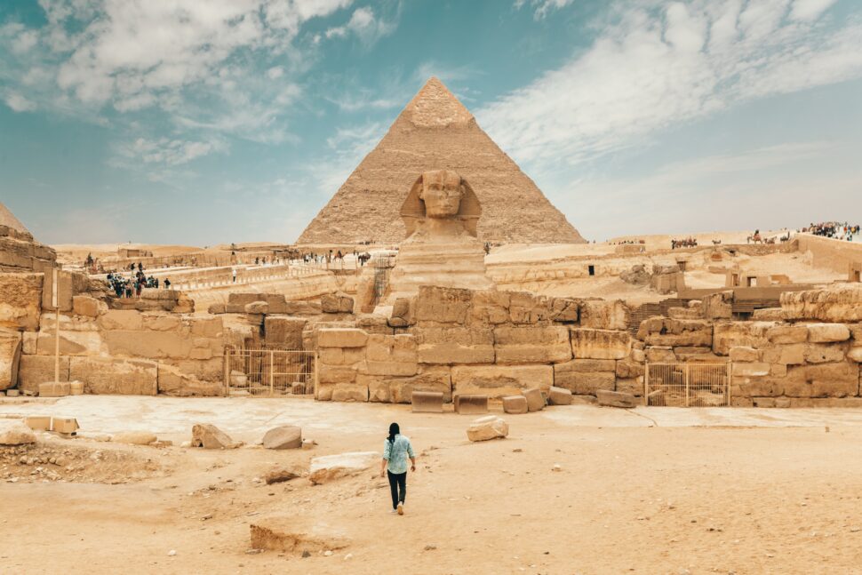 person walking toward the Pharaoh pyramids and ancient Egyptian ruins