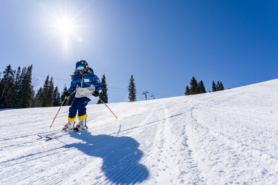 A snow skier heading downhill on the slopes.