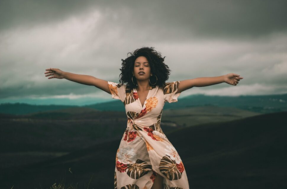 Woman travelers can find solitude in Mauritius and Botswana. Pictured: a Black woman with her arms outspread; behind her is the open sky of Africa.