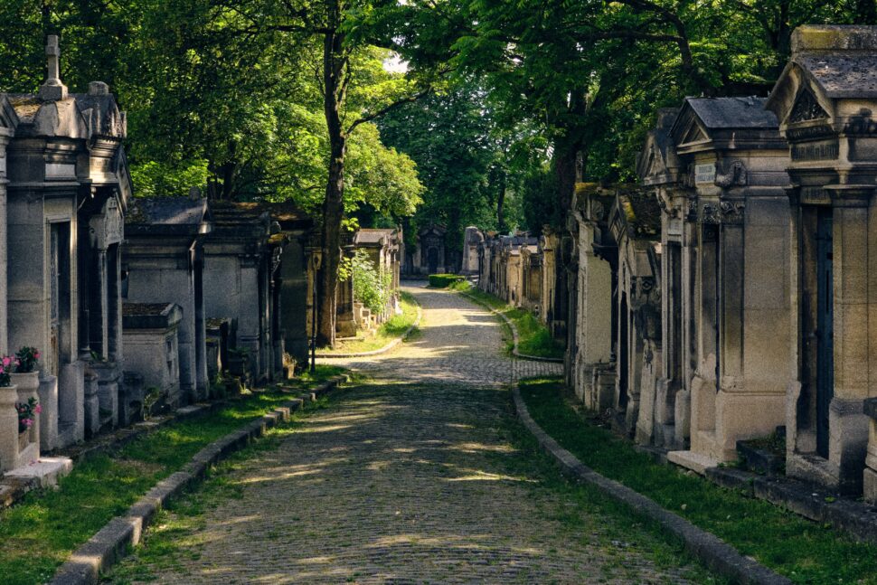 The Père Lachaise Cemetery is a famous burial place in Paris. It is famous due to those resting there and the serene ambiance it provides to visitors who tour and learn more about its history. 
pictured: Père Lachaise Cemetery during a sunny day with overarching trees on the paved road