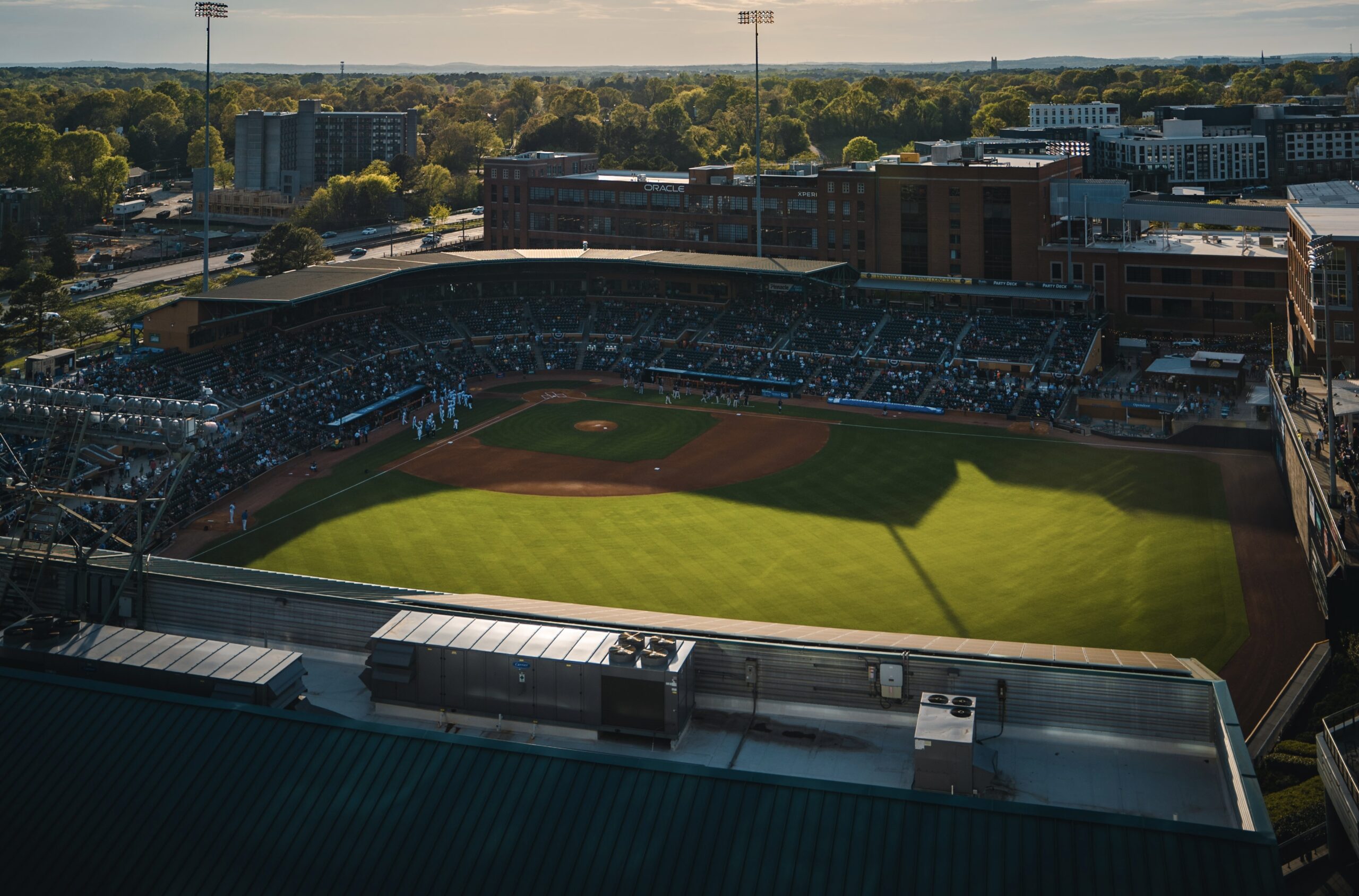 There is a lively sports culture in Greensboro, North Carolina. Learn about the popular sports venues in the charming city. 
Pictured: A North Carolina baseball field on a sunny day with overcast shadows and full seats 