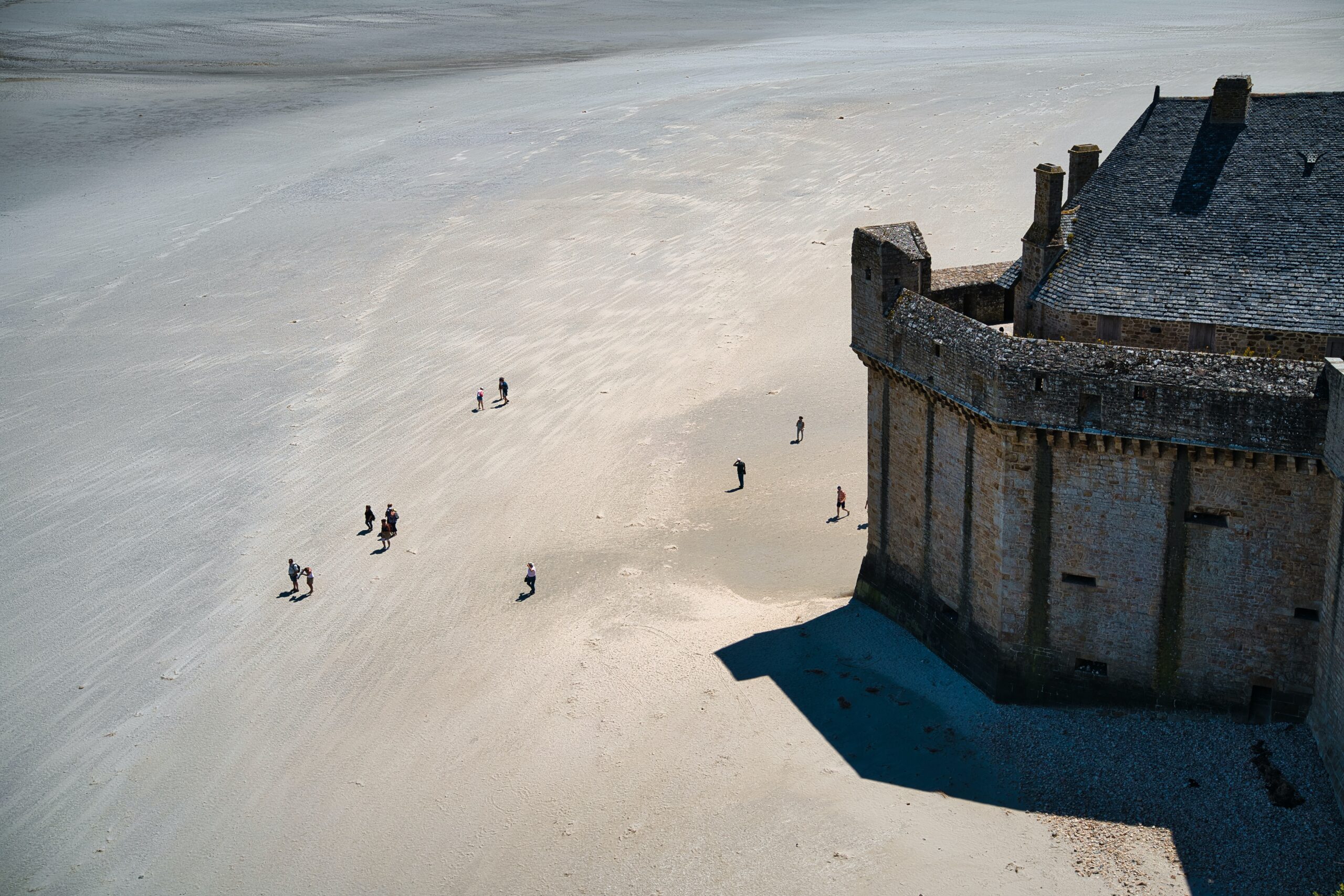 Mont-Saint-Michel is a stunning tourist destination in Normandy.
Pictured: Mont-Saint-Michel during low tide with people exploring the sandbanks seemingly on a walking tour 