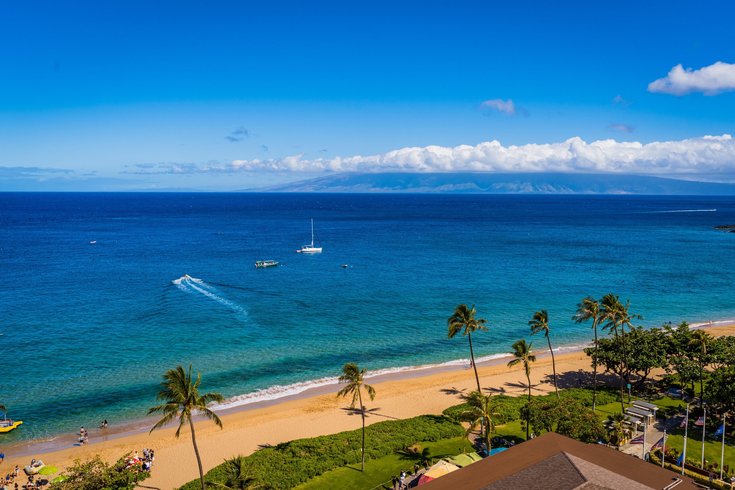 Maui is a beloved island that has many activities for visitors. 
Pictured: The shore of Maui with a oceanfront resort and beach goers 
