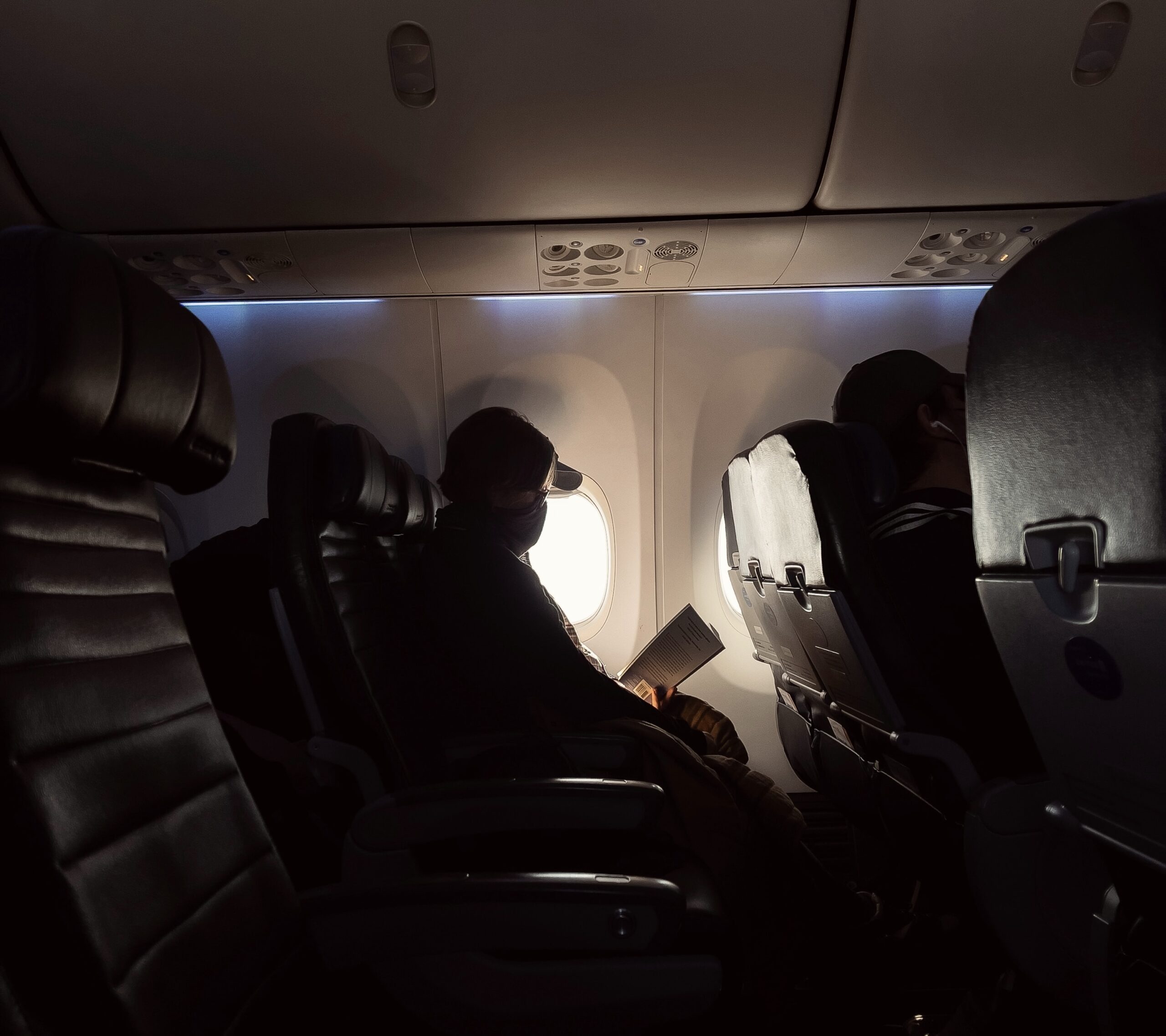 Airlines have had some modern updates to booking and fleets to compete with other airlines. 
Pictured: A man on a dark airplane looking out the bright window with a book in his hand 