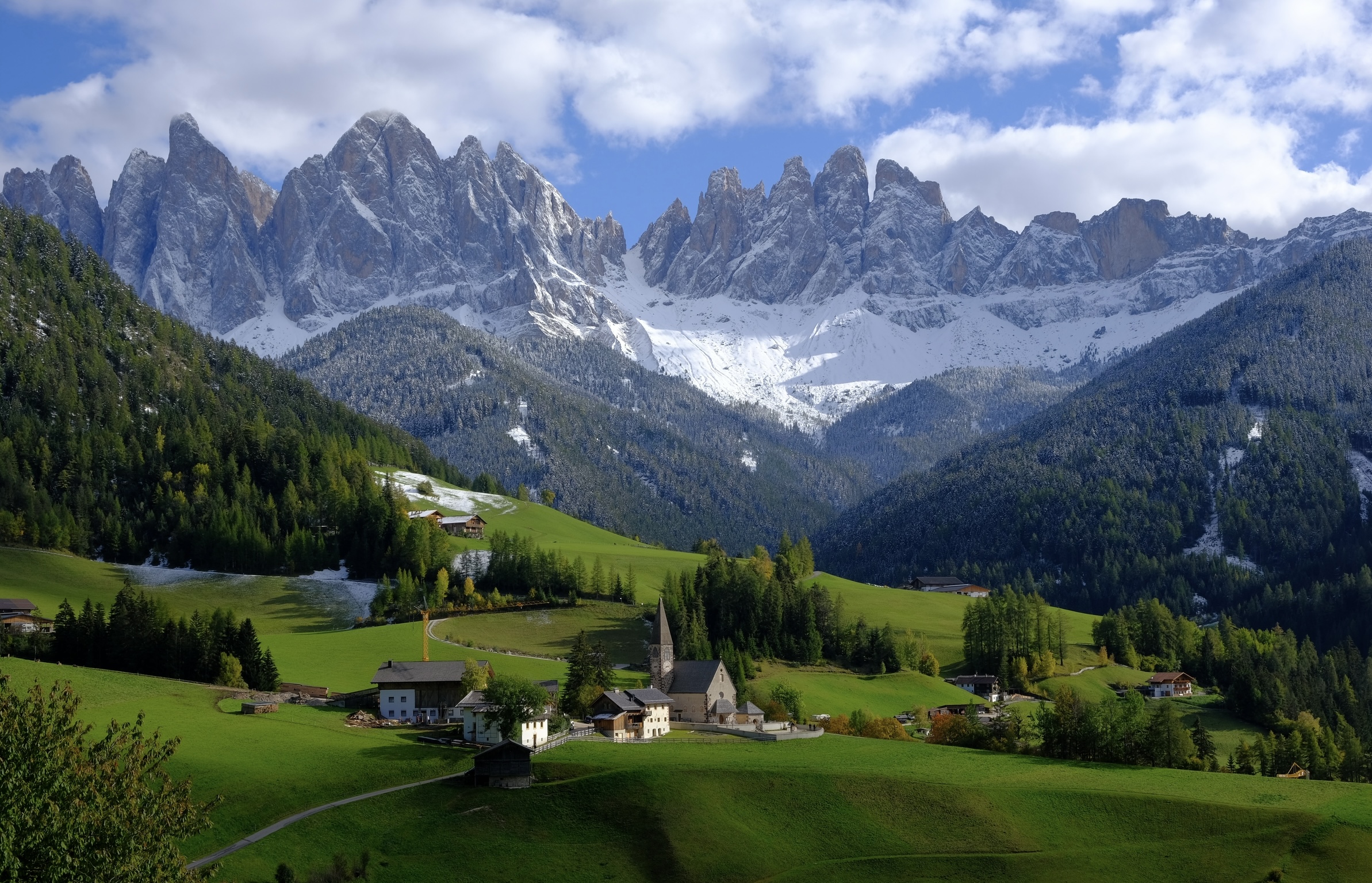 Val Gardena is an area near the Dolomites that many visitors love to stay in. 
Pictured: The lush green valleys of the Dolomites with snowy jagged mountains in the background
