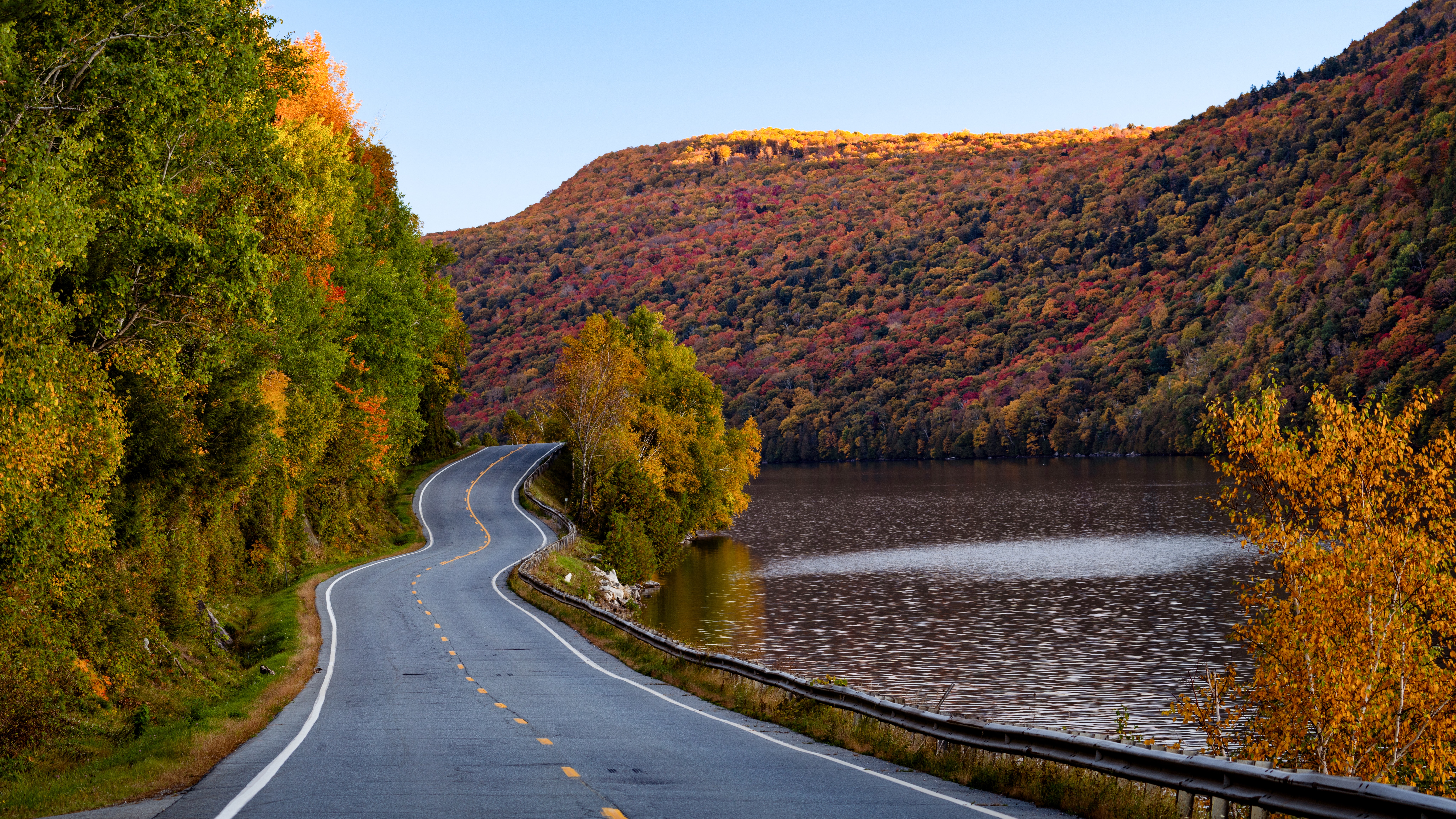 New Hampshire is a small and historic state of New England. Learn more about the state and what there is to do. 
pictured: A winding road in New Hampshire with a rainbow of fall leaves surrounding the nearby river 