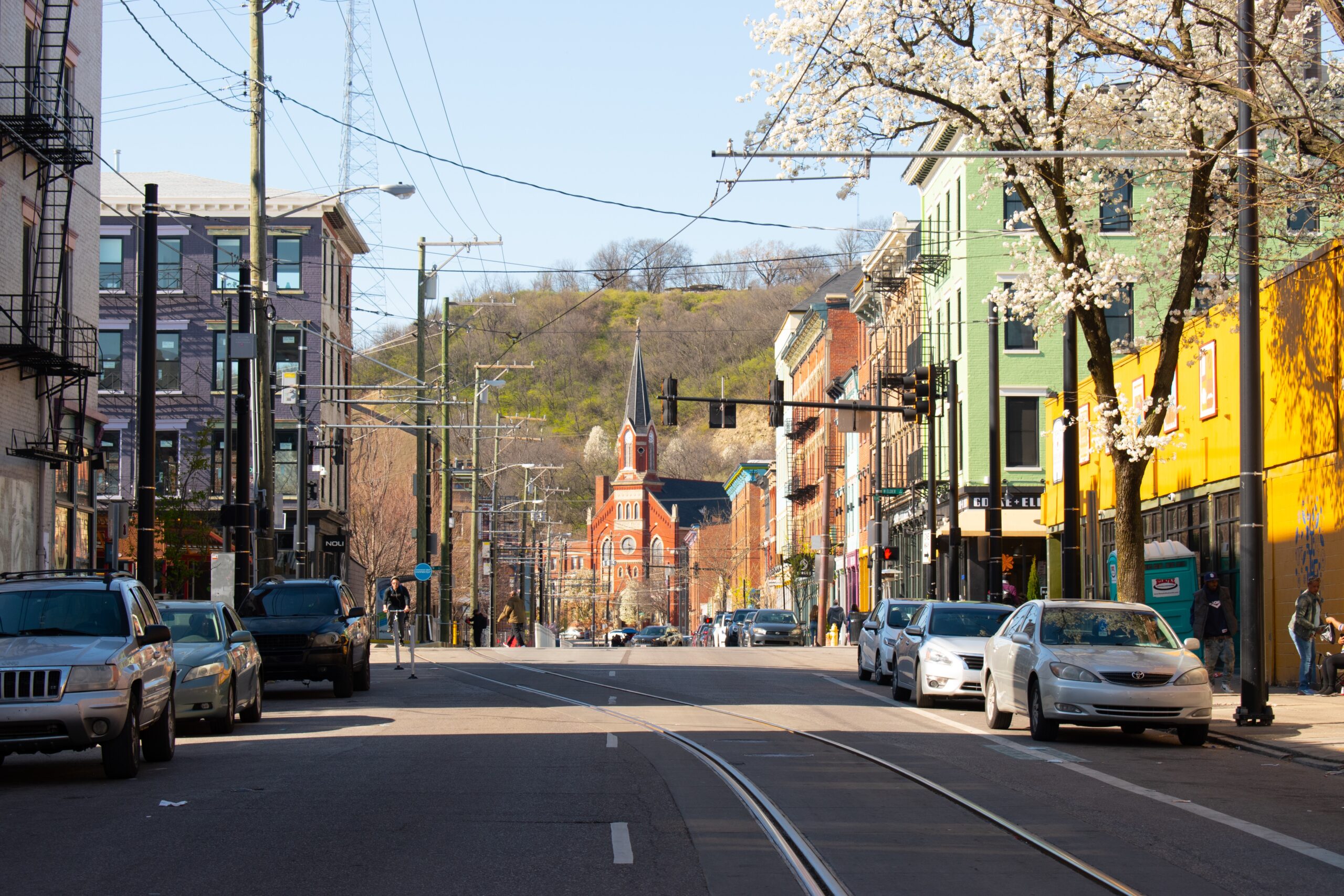 The weather and seasons of Cincinnati can cause trouble for travelers. Learn more about what to steer clear of when visiting the city. 
pictured: a street of Cincinnati with many parked cars and pedestrians on a bright day 