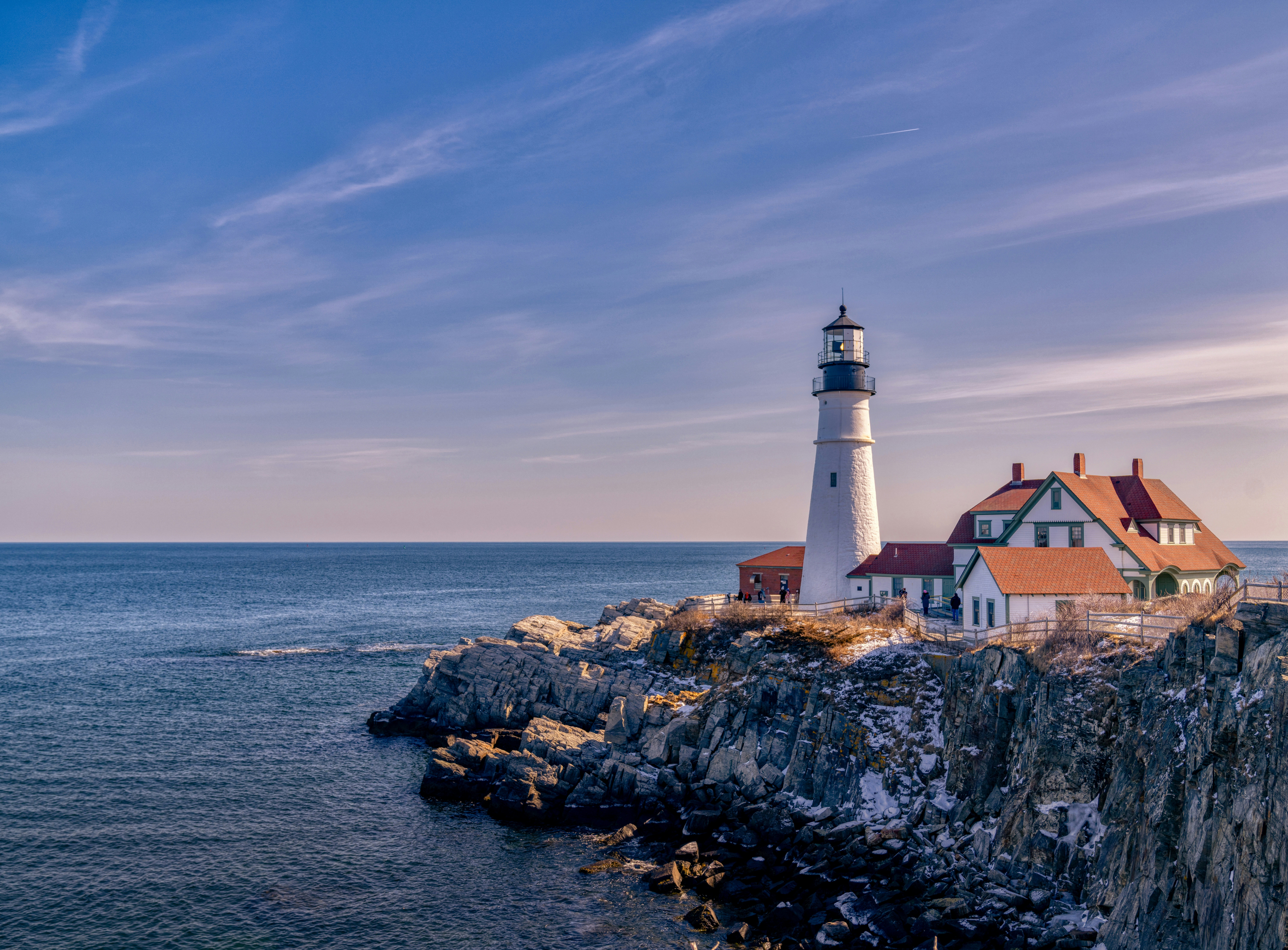 Maine is a coastal state that many love to visit. Learn more about the New England state's offerings.
pictured: a cliff in Maine with a lighthouse and lodging sitting near the rocky edges