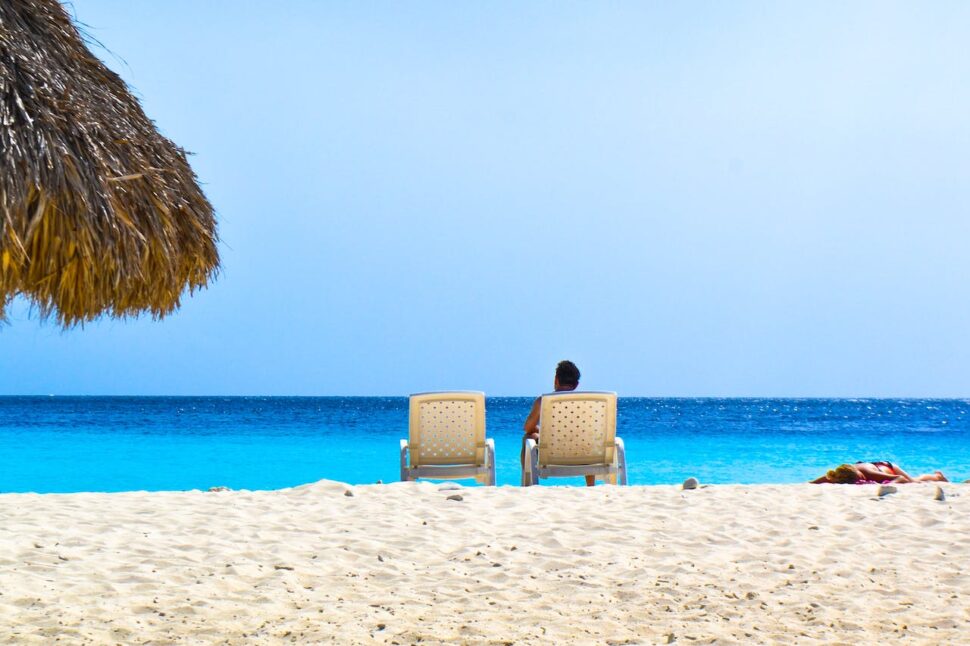 A person sitting in a beach chair with another one beside him on a beach in Curaçao.