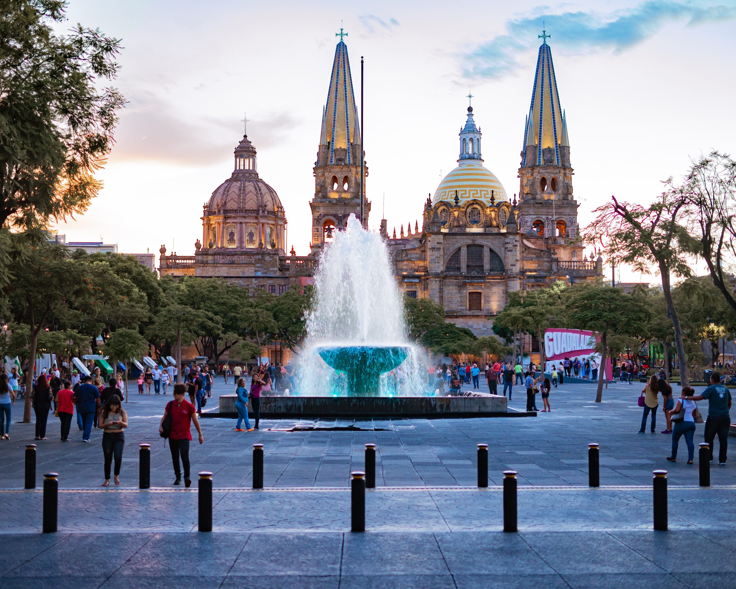 Travelers of Guadalajara should be sure to research the area before traveling to ensure their safety. 
pictured: The city center of Guadalajara complete with a tourism sign with the cities name and fountain that pedestrians walk around 