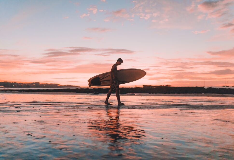 A man walking along the beach with a surfboard at sunset in Tamarindo.
