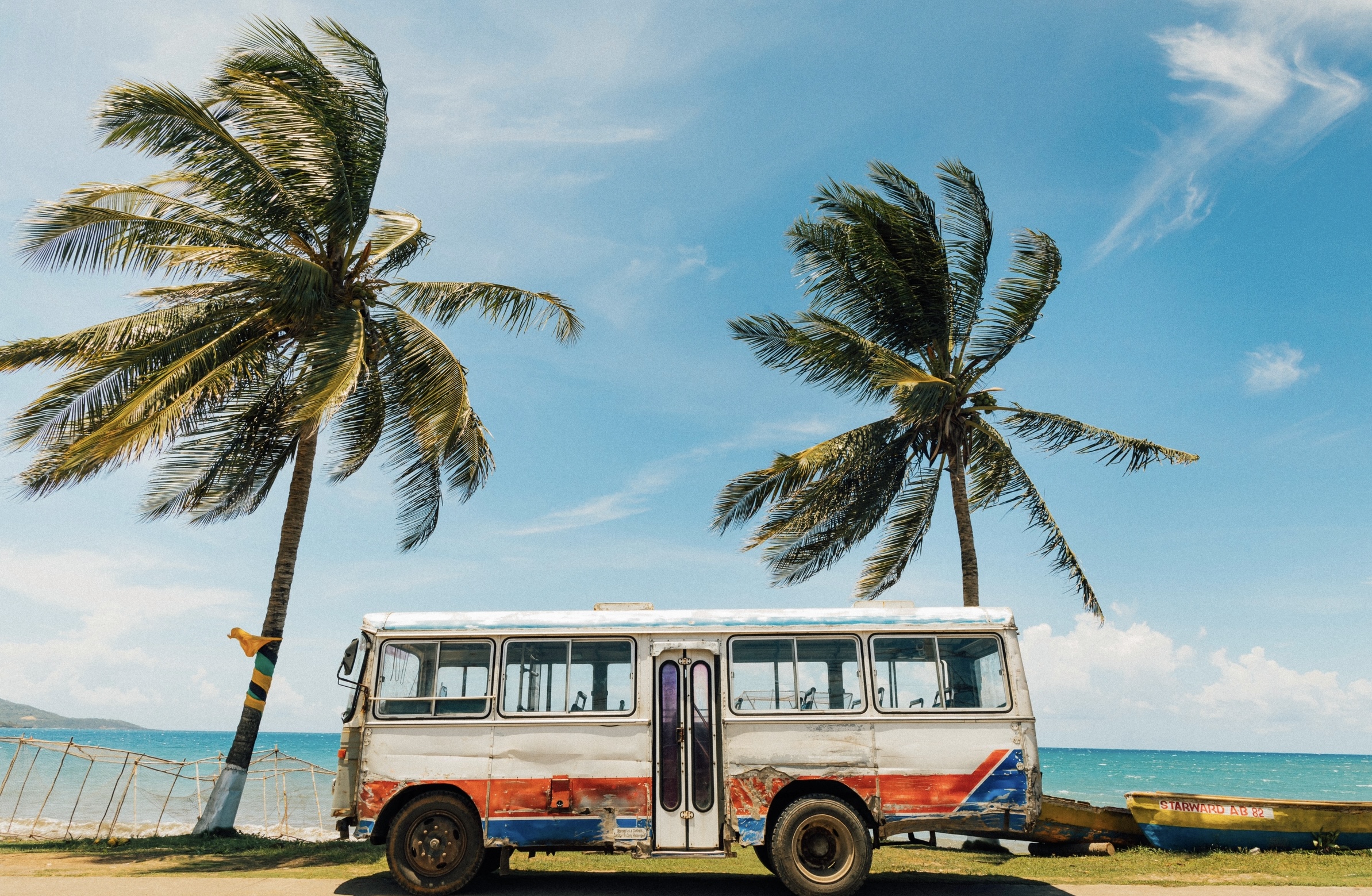 Jamaica is a hot destination that can make the best winter vacation location, during January. 
Pictured: a Jamaican beach with large palm trees, clear waters and a retro bus 