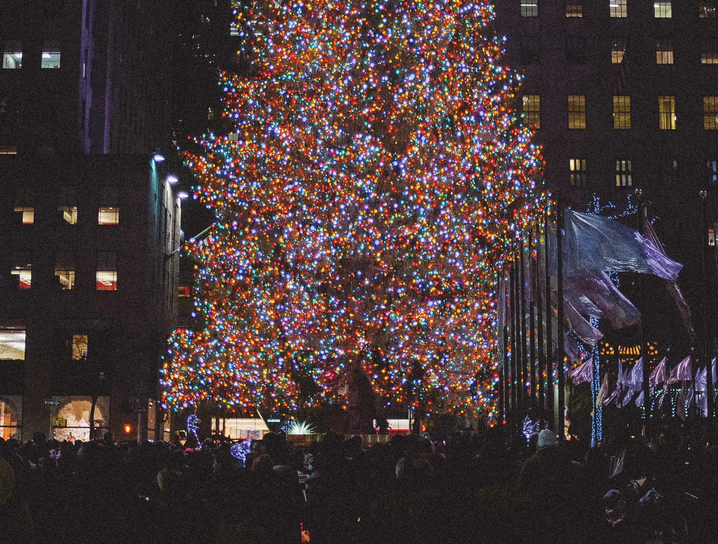 The Rockefeller Christmas Tree is a well celebrated trademark of NYC during the holidays.
Pictured: people surrounding the Rockefeller Christmas Tree  at night while it is lit up with Christmas lights 