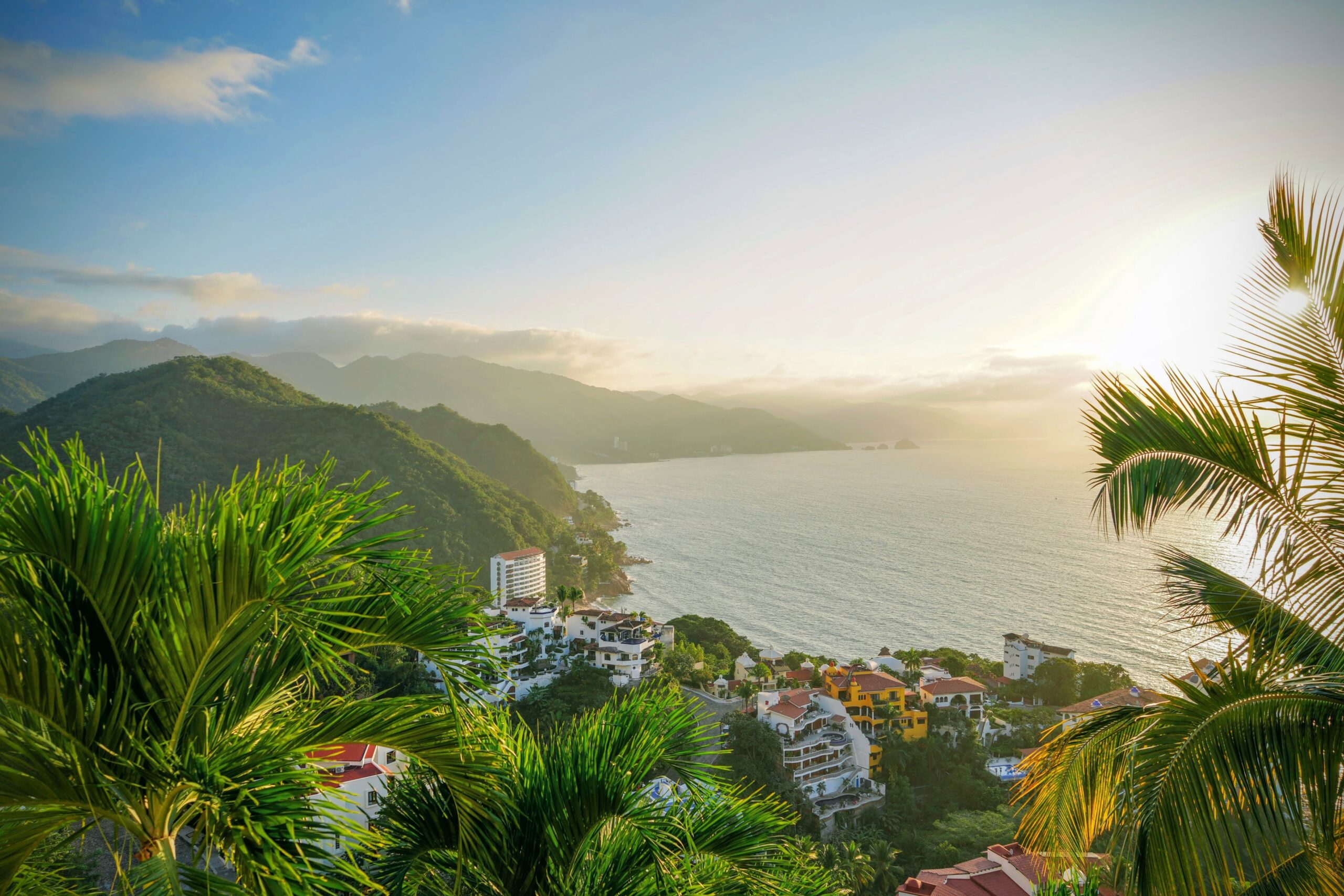 Travelers should consider a trip to Puerto Vallarta for a safe yet exciting tropical trip.
Pictured: the coast of Puerto Vallarta during sunset with a vibrant forest and town 