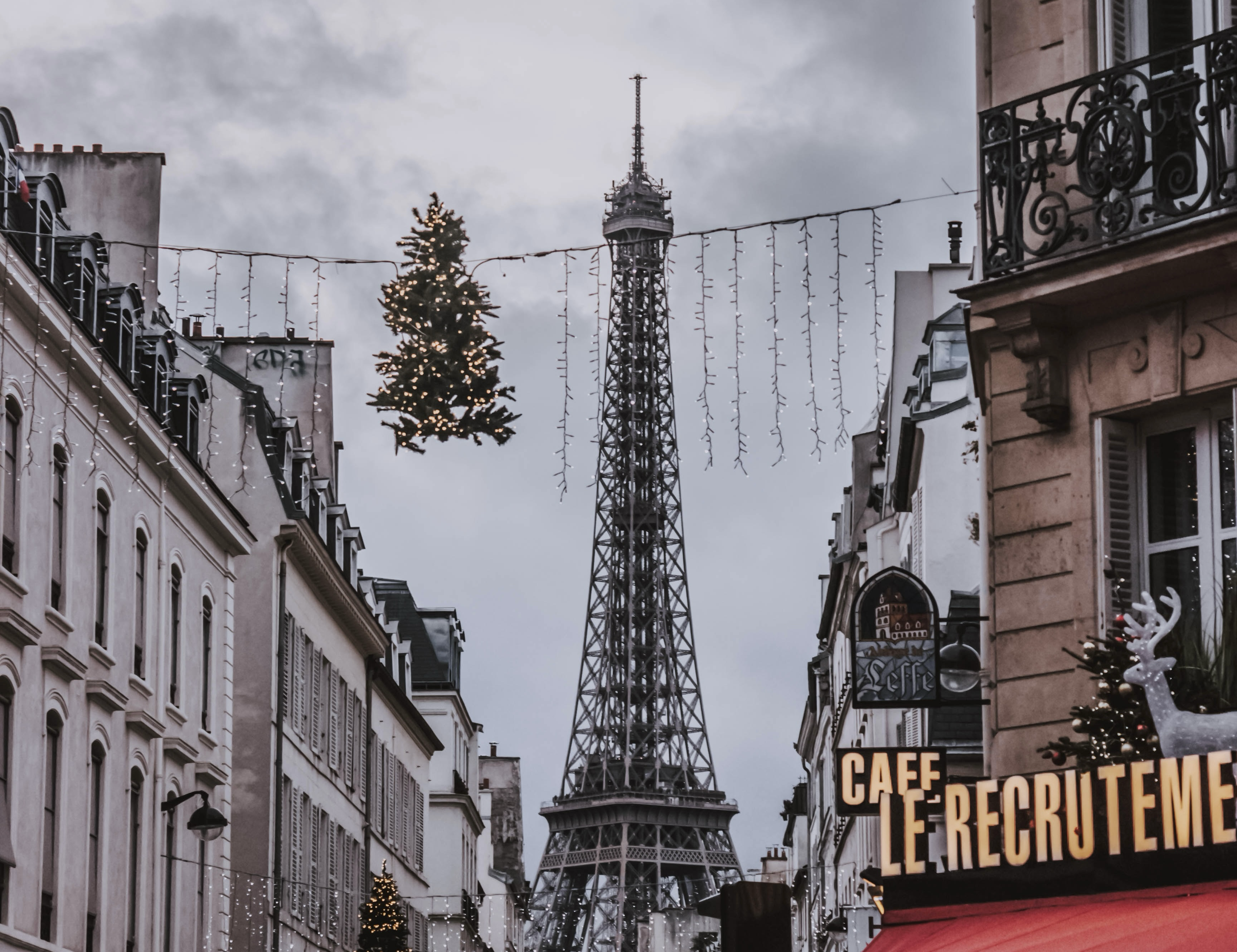 Visit the romantic city with the most stunning sights and activities, like the market, during the holidays. France is the perfect holiday destination. 
Pictured: France’s streets decorated with Christmas lights and trees hanging in front of the Eiffel Tower 