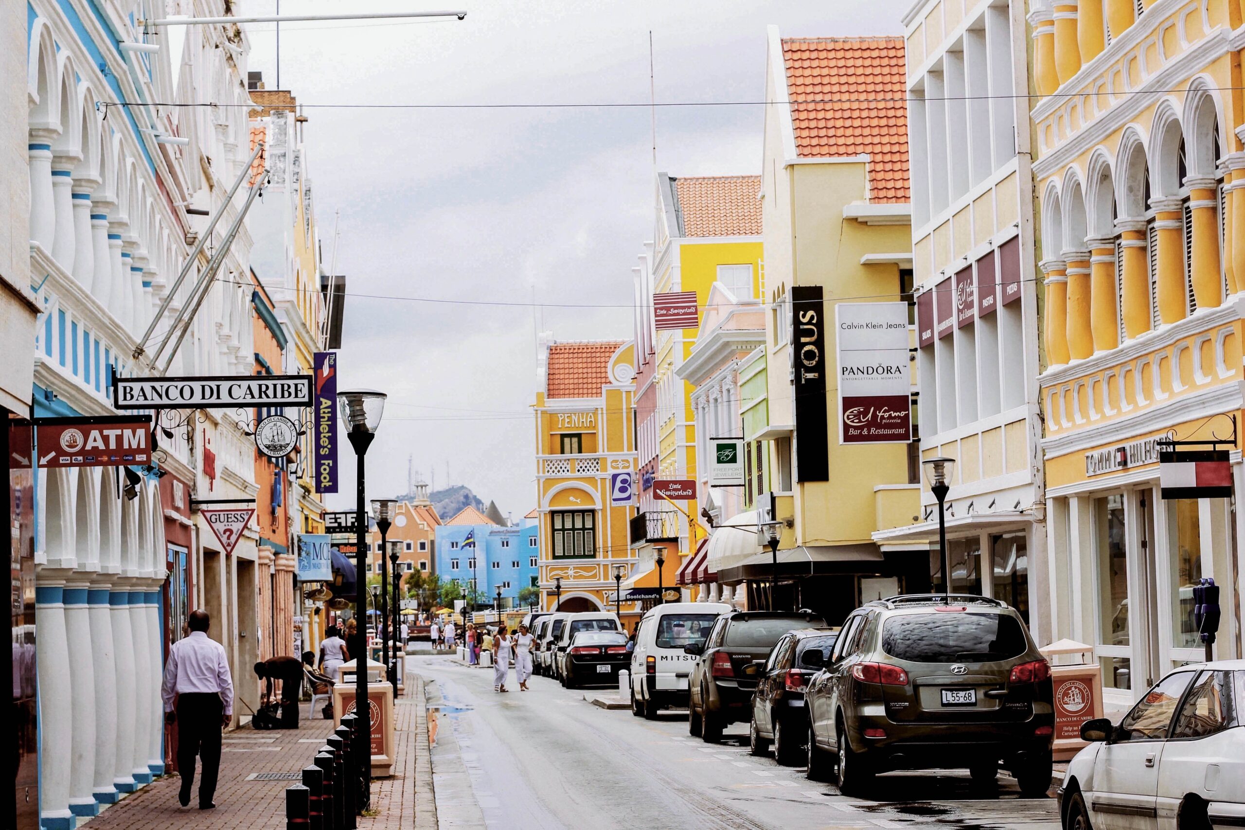 The city of Curaçao is quaint and has welcoming community. The island is a  safe place for travelers and has a thriving culture. 
pictured: the downtown area of Curaçao with pedestrians walking from shop to shop and cars parked on the street