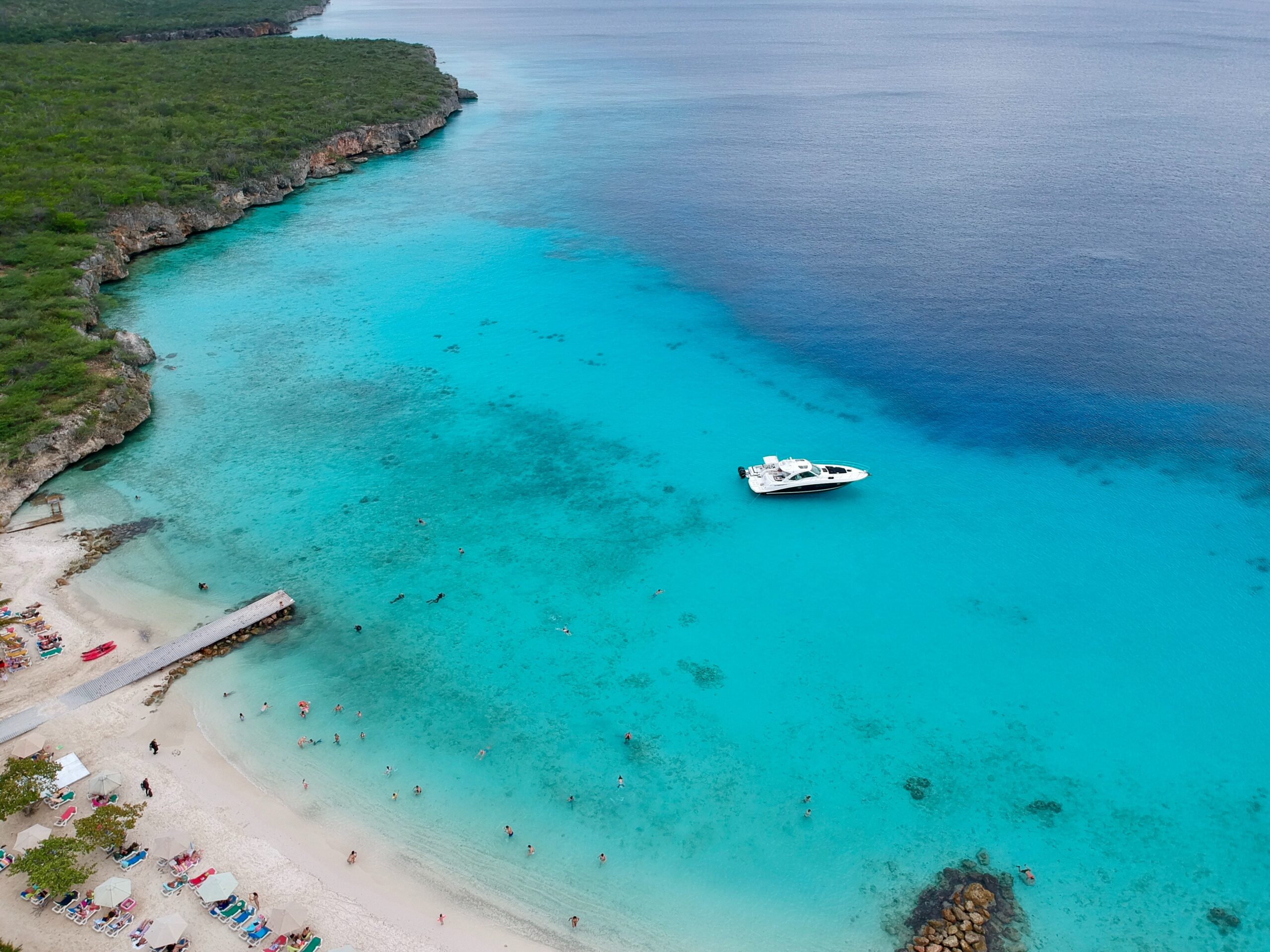 Curaçao is a unique Caribbean island that can be the perfect tropical destination for an upcoming trip. Learn more about the thriving culture and safety level of the island. 
pictured: one of Curaçao's coast lines with people enjoying boating and beach fun 