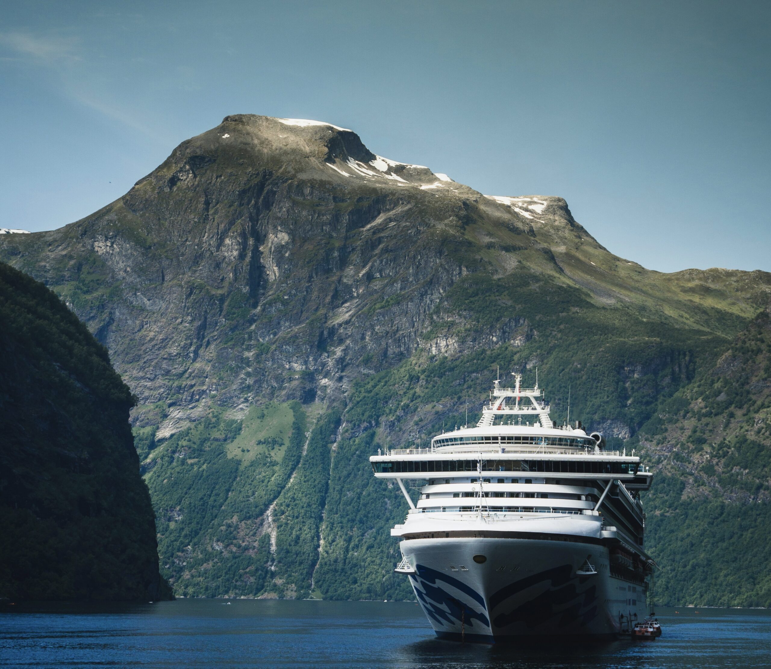Life at Sea cruises have received negative feedback due to the last minute cancellation of the three year long cruise. 
Pictured: a cruise ship in front of a grand mountain on a bright blue day 