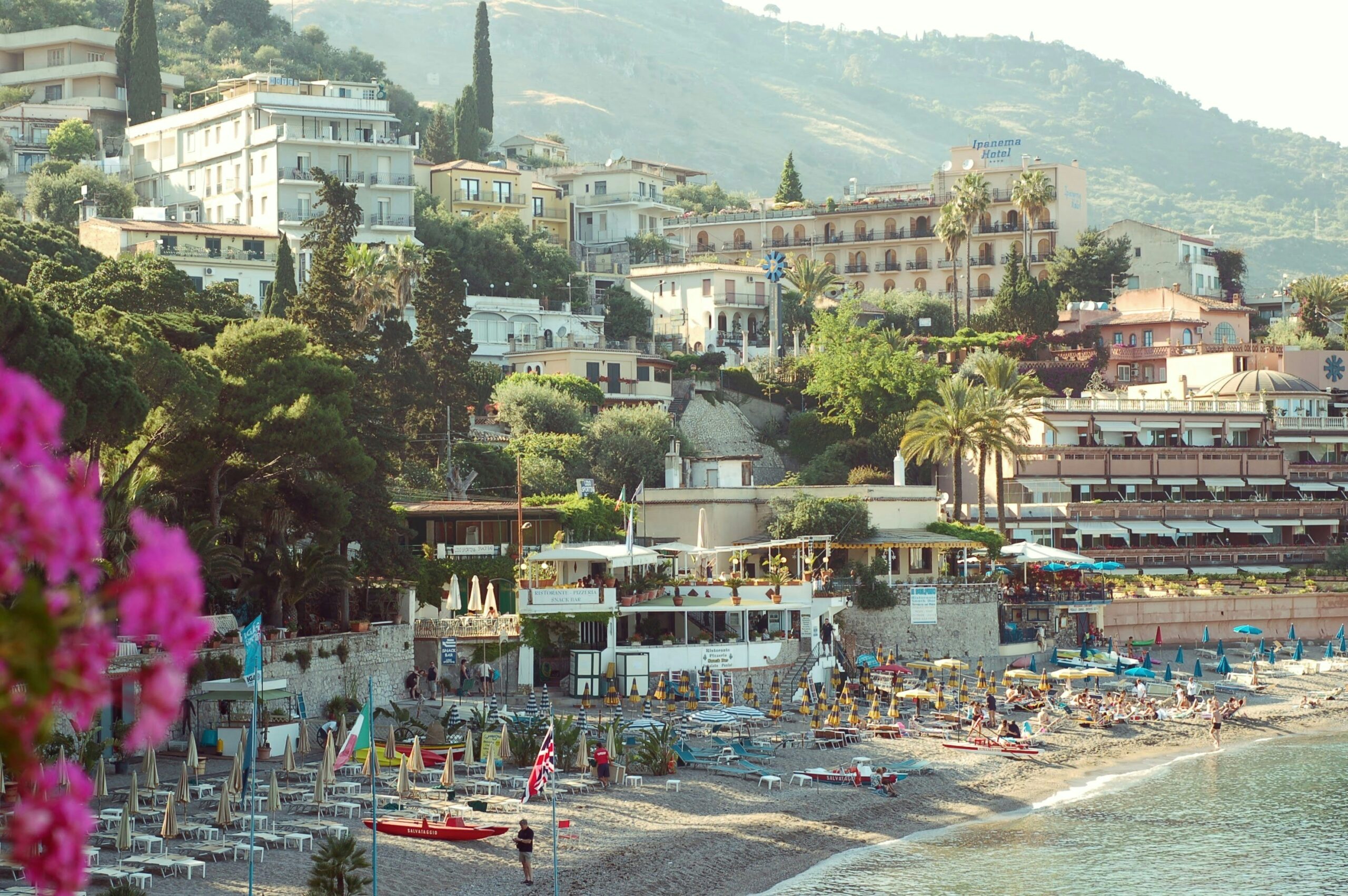 These activities in Taormina are the top offerings for tourists. 
pictured: a lively beach of Taormina with lush greenery and clear waters