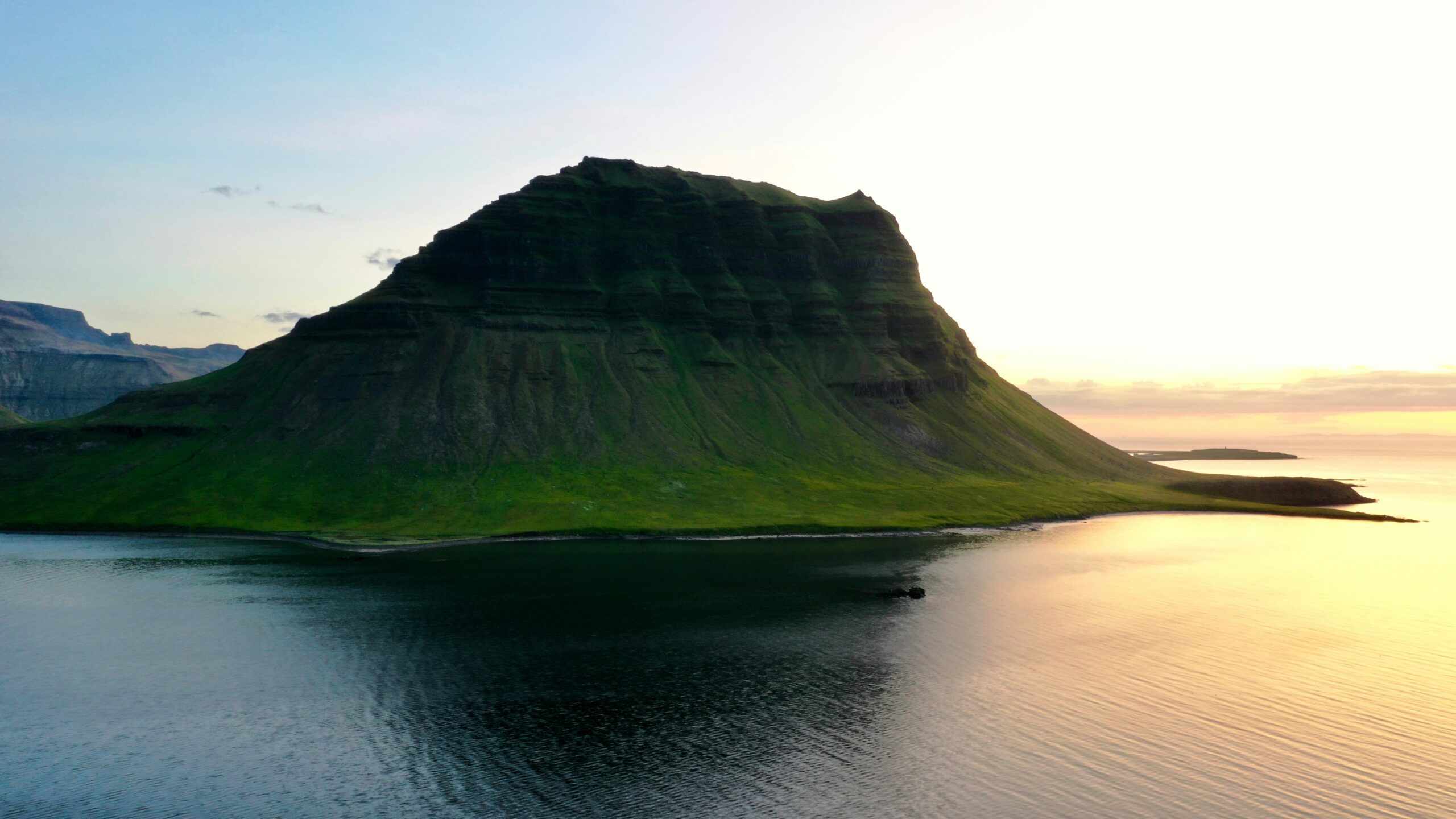 The Midnight Sun is a phenomenon in Iceland that travelers will not miss if they visit in August.
pictured: a lush green mountain during sunset in Iceland